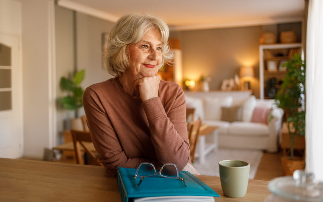 Thoughtful senior woman sitting at table with photo album and coffee cup while contemplating memories at home
